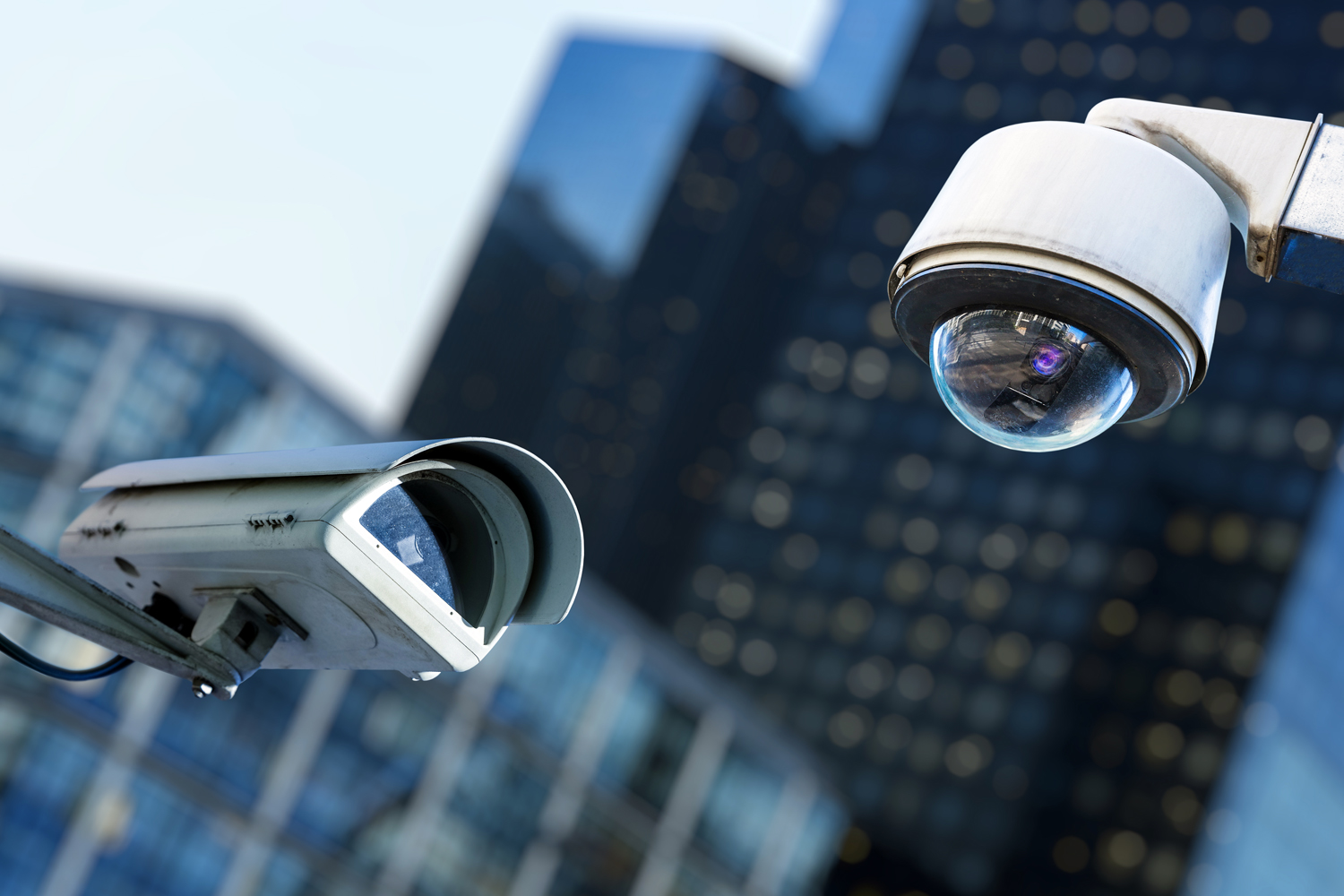 two cctv security camera in a city with blury business building on background