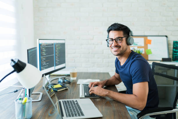 Smiling young Latin male freelance programmer sitting with technology at desk